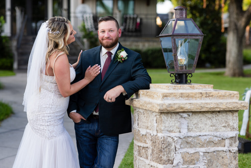 Groom leaning against light post with legs crossed and bride standing with hand on hip smiling at groom