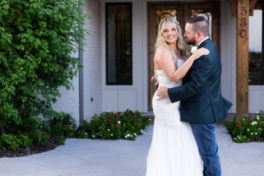 Groom looking at bride while she smiles over shoulder in front of hotel entrance