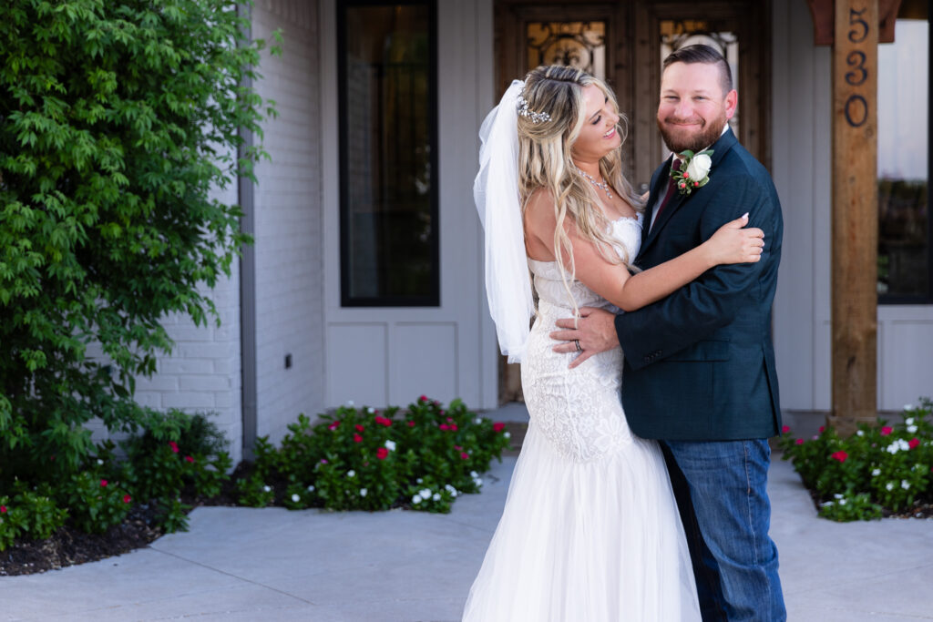 Bride looking at groom while he smiles at camera in front of hotel entrance