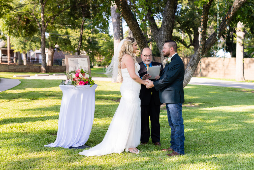 Bride and groom holding hands during intimate elopement wedding ceremony on lawn at Hotel Lucy in Granbury TX