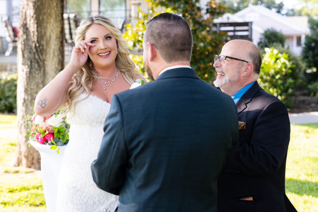 Bride wiping tear while smiling during outdoor intimate elopement ceremony