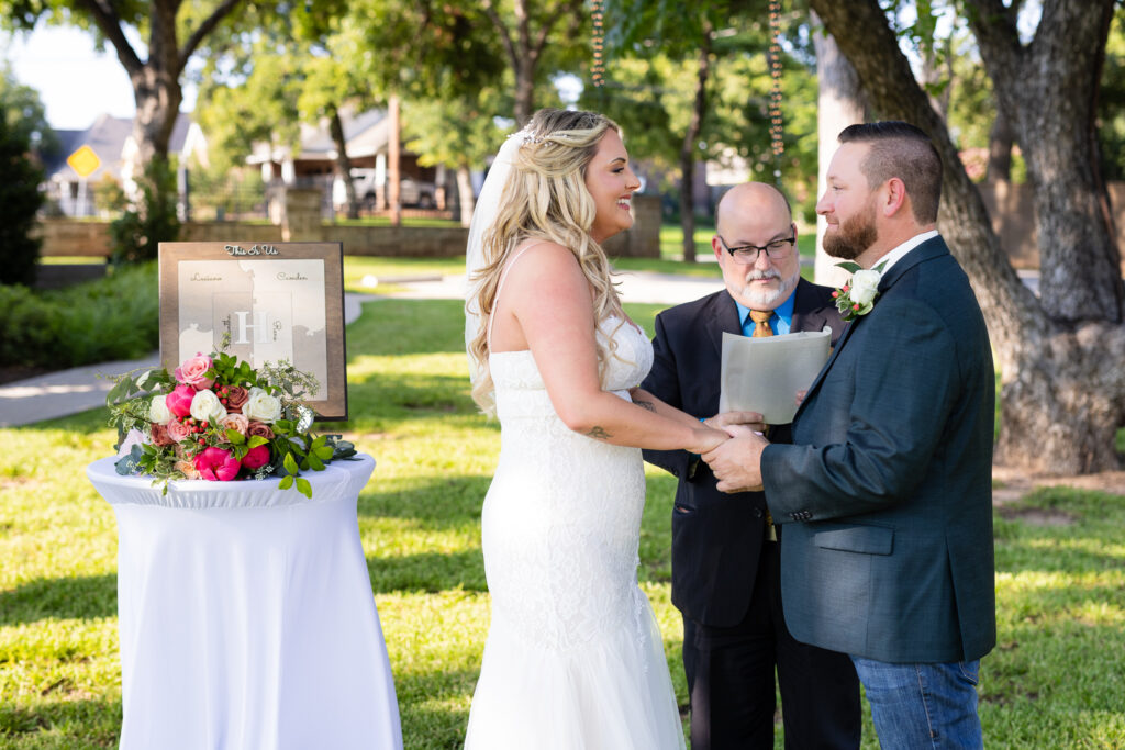 Bride and groom smiling and holding hands during intimate elopement wedding ceremony on lawn at Hotel Lucy