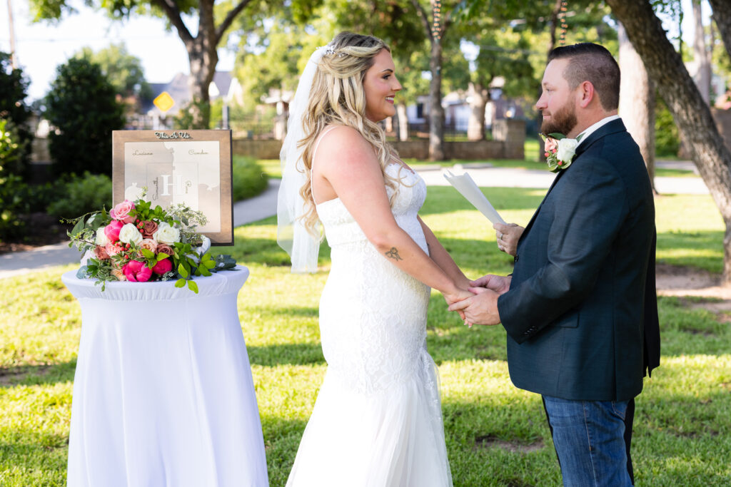 Bride and groom smiling and holding hands during intimate elopement wedding ceremony on lawn on hotel lawn in Granbury