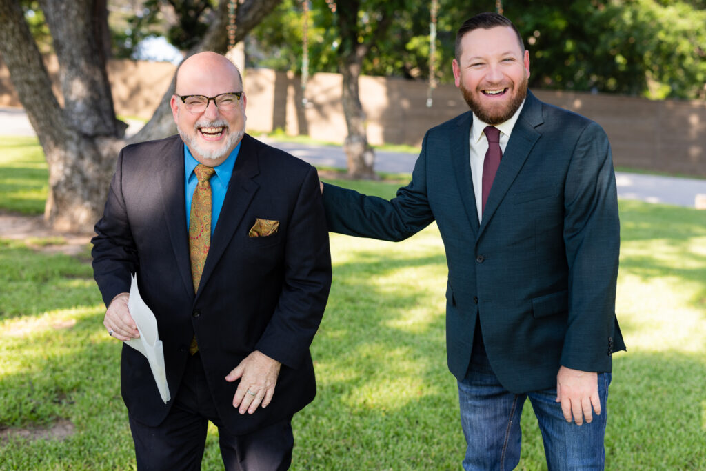 Groom laughing with officiant on lawn before wedding ceremony