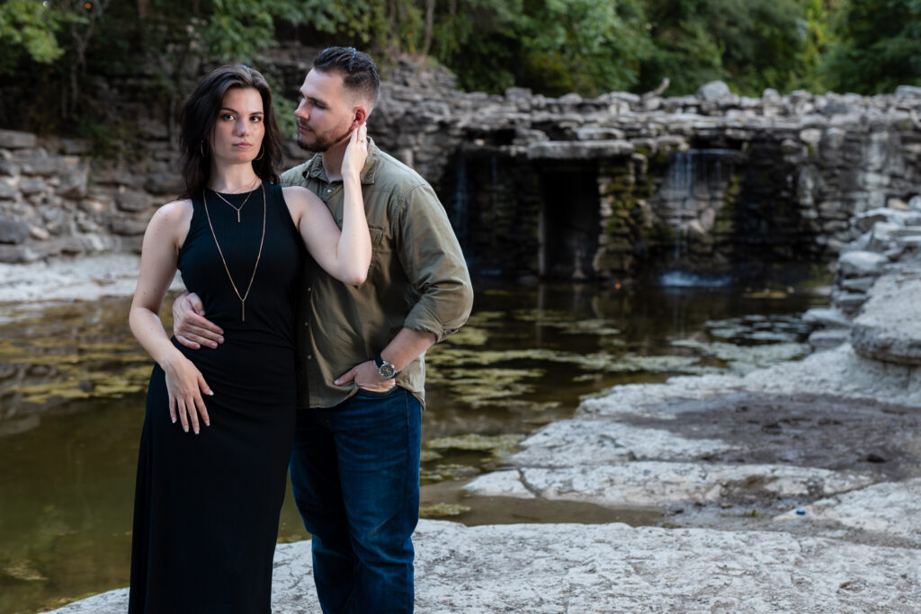 Engaged couple intimately standing together in front of epic stoned waterfall in Richardson TX during engagement session