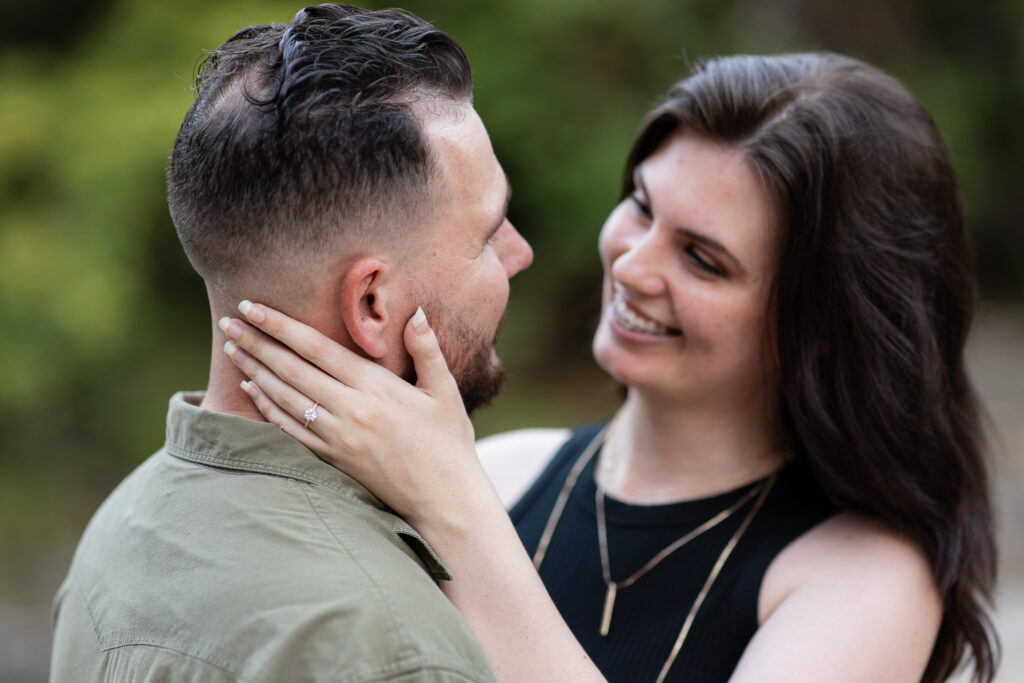 Engaged woman intimately holding fiancé's neck while smiling and showcasing her engagement ring