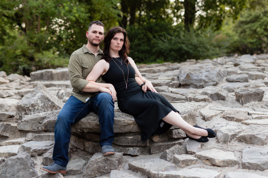 Engaged couple sitting together on a large stone during engagement session at a park in Richardson TX