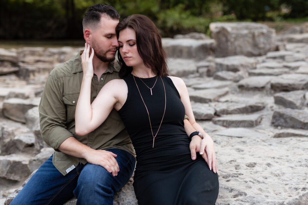 Engaged couple intimately sitting together on a large stone pathway during engagement session at a park in Richardson TX