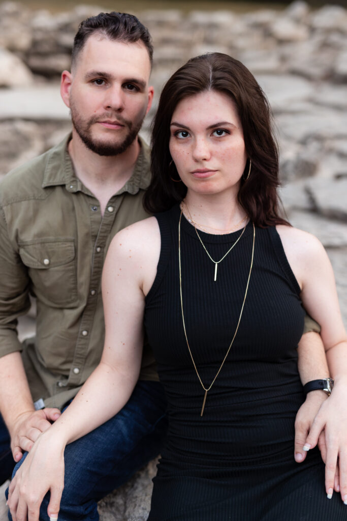 Engaged couple sitting together surrounded by light colored stones during engagement session at a park in Richardson TX