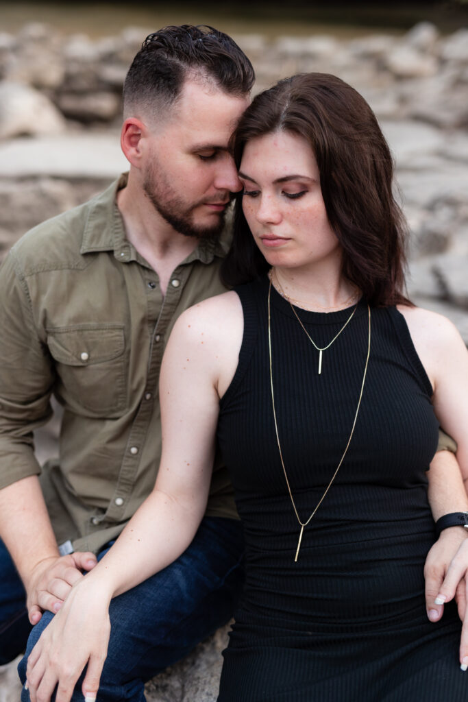 Engaged couple sitting together surrounded by light colored stones during engagement session at a park in Richardson Texas