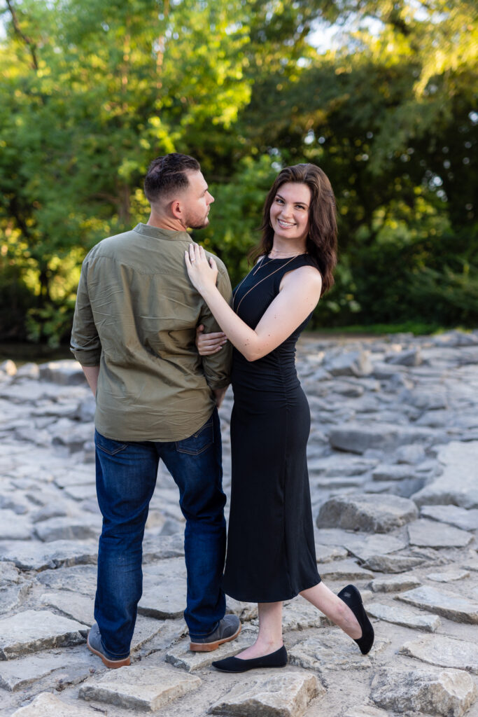 Engaged woman smiling at camera while leaning on fiancé while on stone pathway at Richardson Park