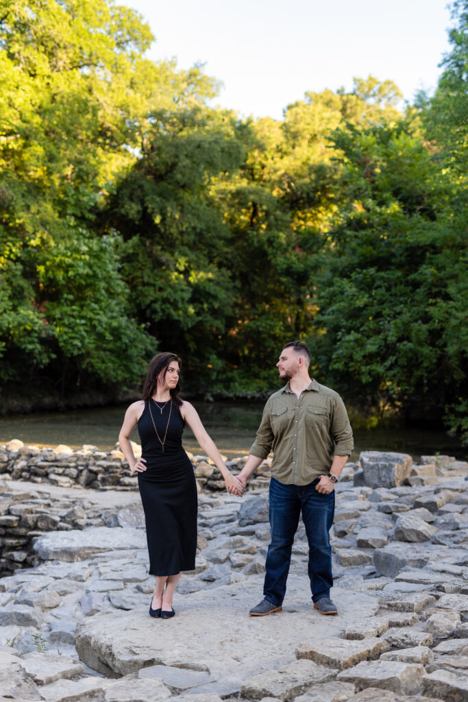 Engaged couple holding hands looking at each other on stone pathway surrounded by lush trees during beautiful Richardson Park engagement session