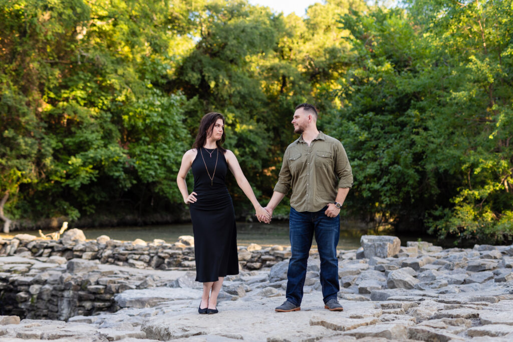 Engaged couple holding hands looking at each other on stone pathway surrounded by lush trees during beautiful Richardson Park TX engagement session