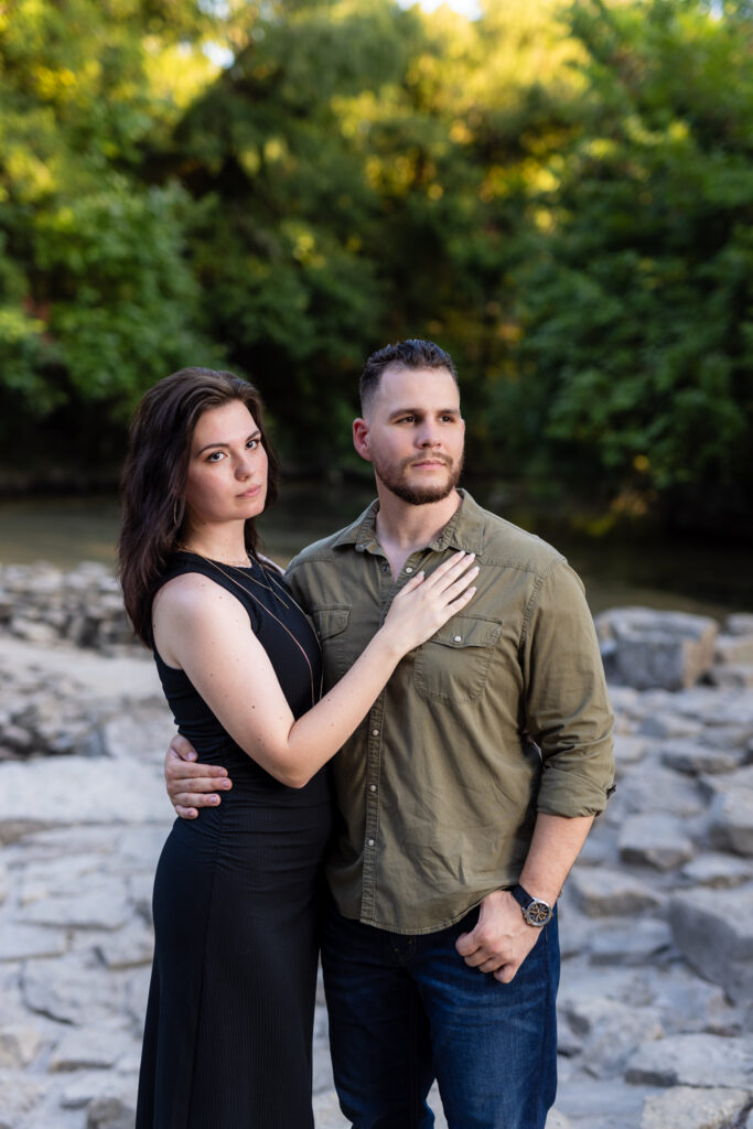 Engaged woman with hand on fiancé's chest surrounded by stones and trees during Richardson Park engagement session in Texas