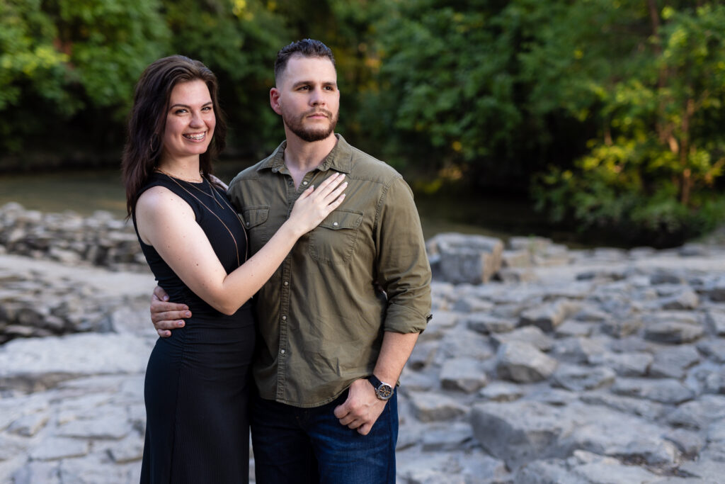 Smiling engaged woman with hand on fiancé's chest surrounded by stones and trees during Richardson Park engagement session in Texas