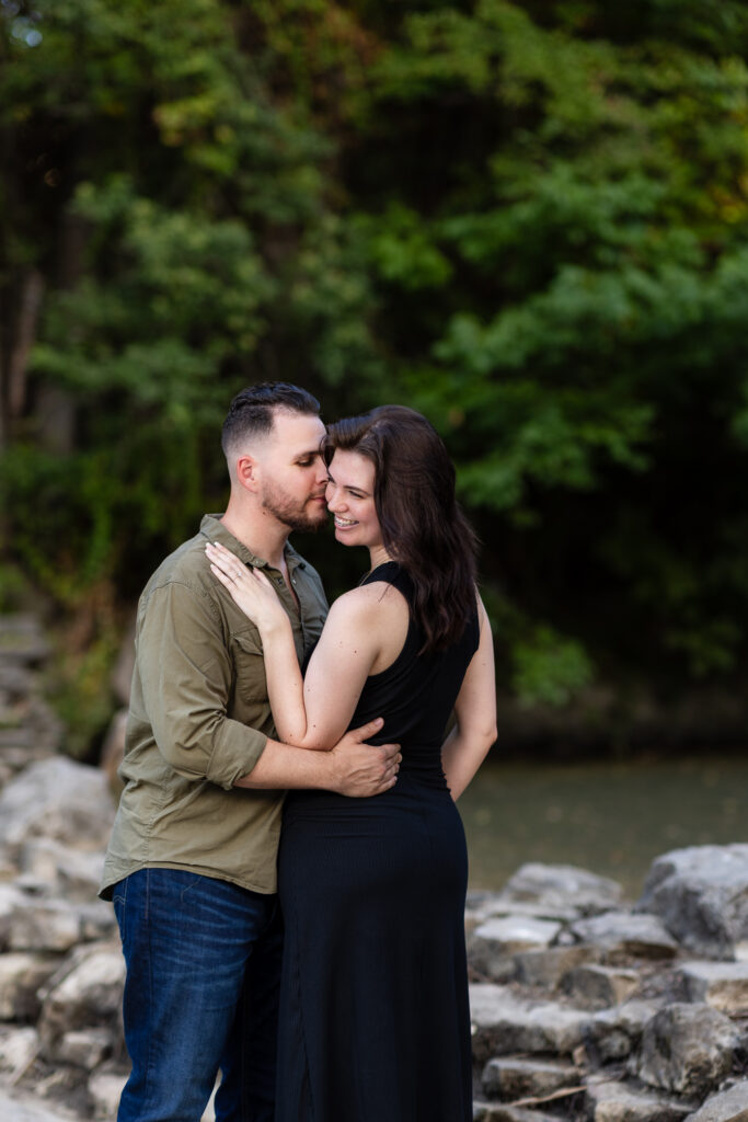 Engaged couple nuzzling intimately standing on stones surrounded by trees during Richardson Park engagement session in Texas