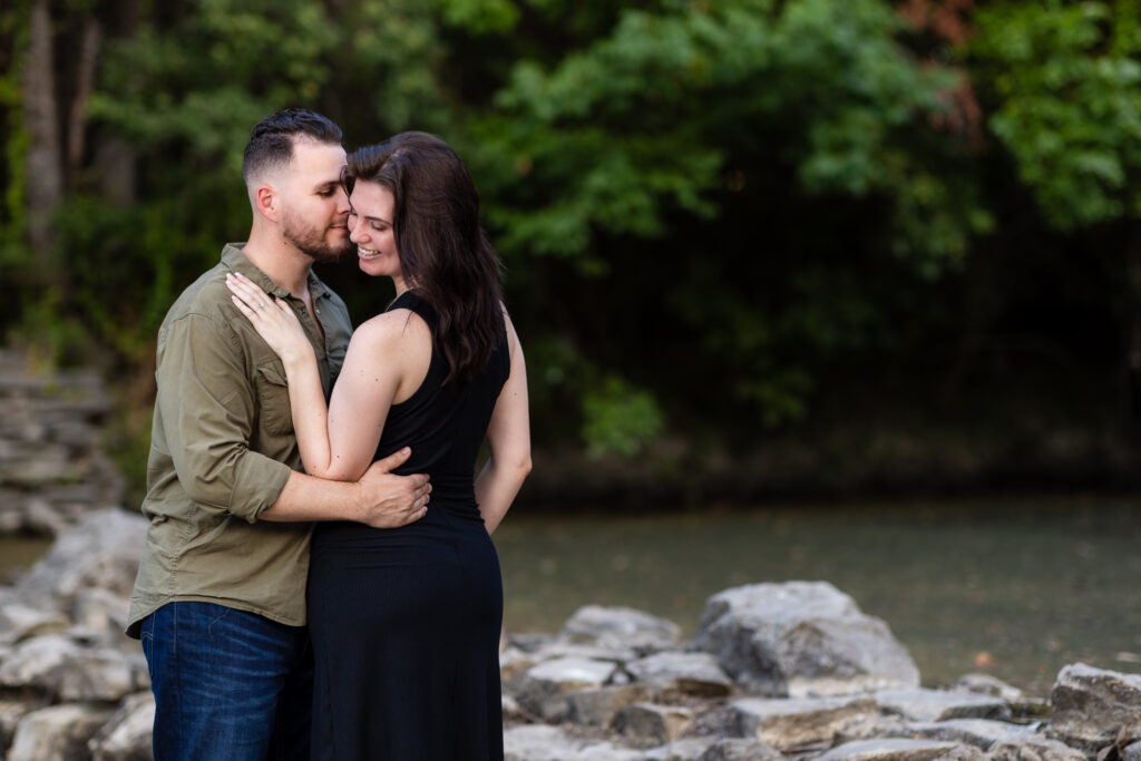 Engaged couple nuzzling intimately standing on stones surrounded by trees during Richardson Park engagement session in TX