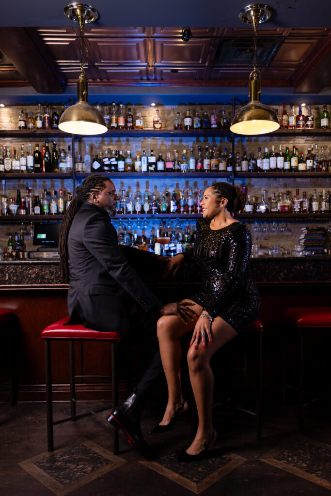 Married man and woman sitting on stools at bar while looking at each other at Thompsons Bookstore Speakeasy during anniversary session