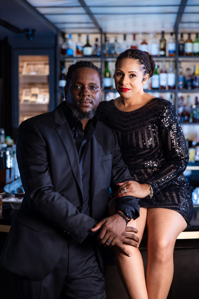 Man standing next to woman sitting on bar during anniversary session at Thompsons Bookstore Speakeasy in downtown Fort Worth