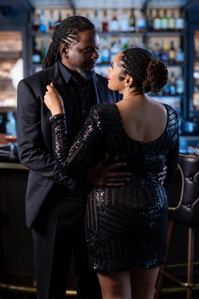 Woman leaning against man's chest in all black during romantic anniversary portrait session at Thompsons Bookstore Speakeasy in downtown Fort Worth