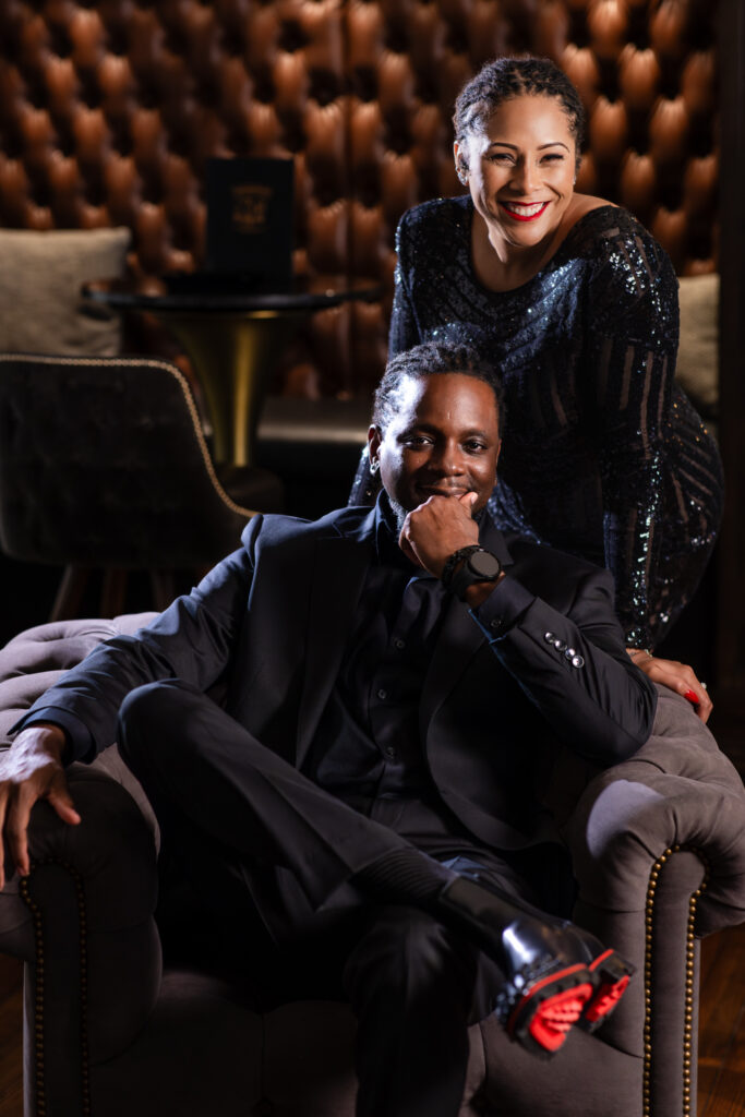 Man sitting in chair revealing red bottom boots while woman leans behind in all black during anniversary photo session