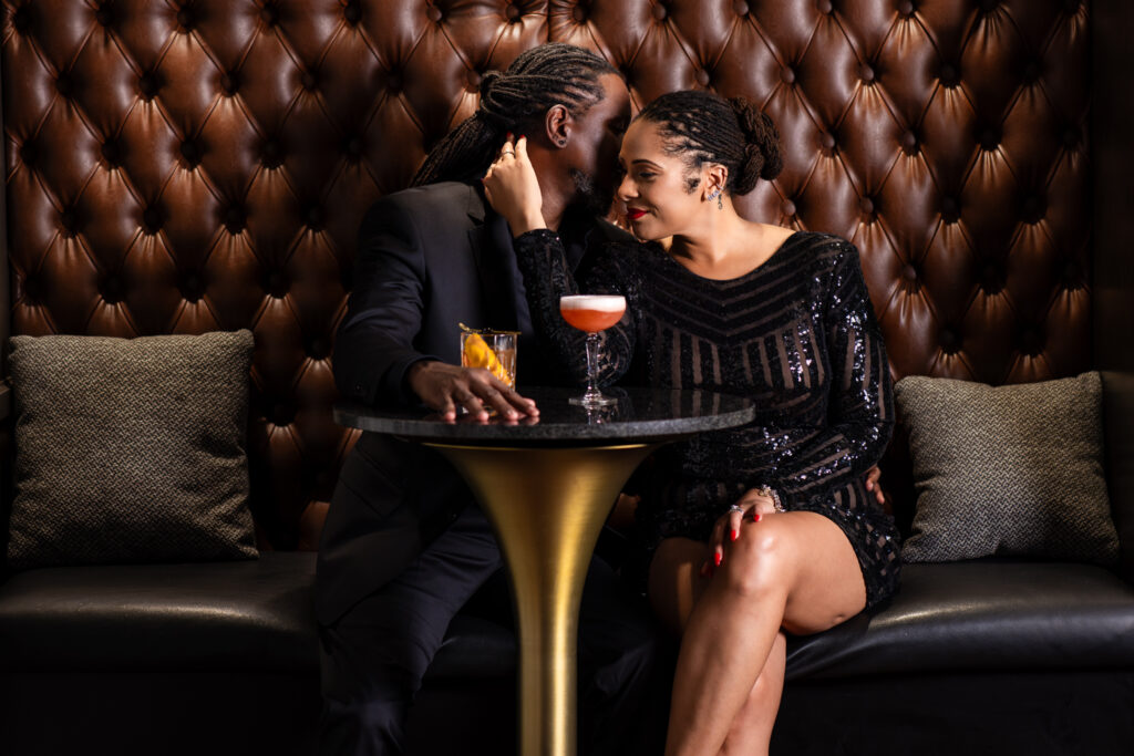 Man whispering intimately into woman's ear while sitting together at a cocktail table