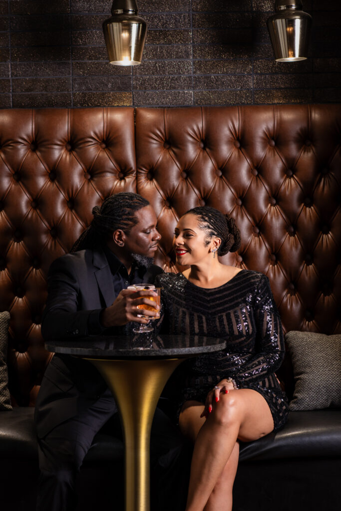 Man and woman smiling at each other while sitting together at a cocktail table at a FW speakeasy