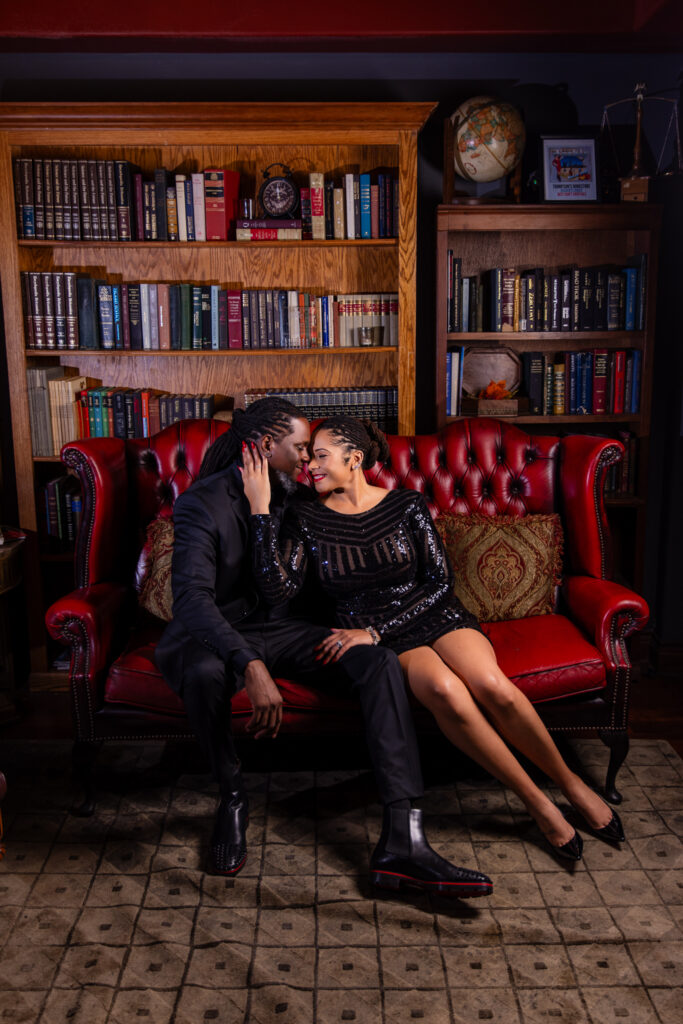 Woman sitting close to man foreheads together on red couch in unique speakeasy in downtown Fort Worth during anniversary session