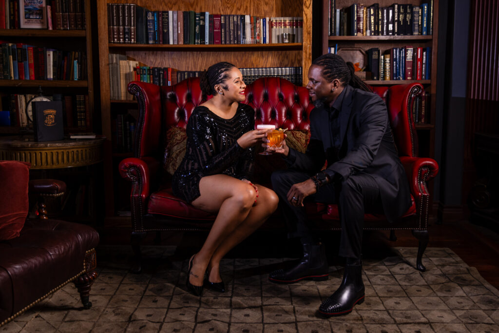 Woman toasting with a man smiling at each other on red couch in vintage speakeasy in downtown Fort Worth