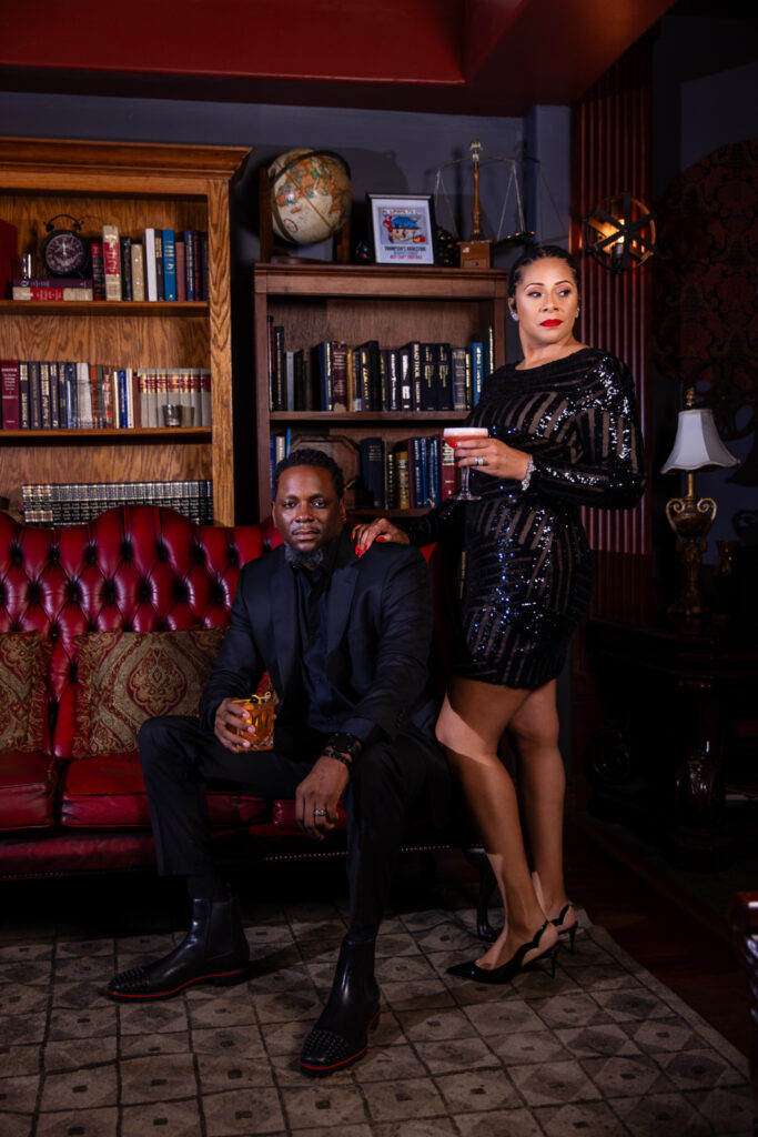 Woman standing next to man sitting on red couch holding cocktails and wearing all black in unique vintage speakeasy in Fort Worth