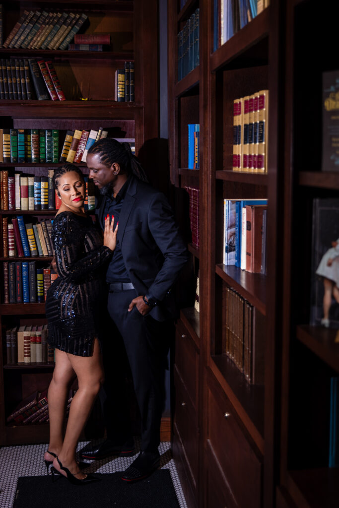 Woman leaning up against man amidst book shelves wearing all black during unique anniversary session at Thompsons Bookstore Speakeasy in downtown Fort Worth