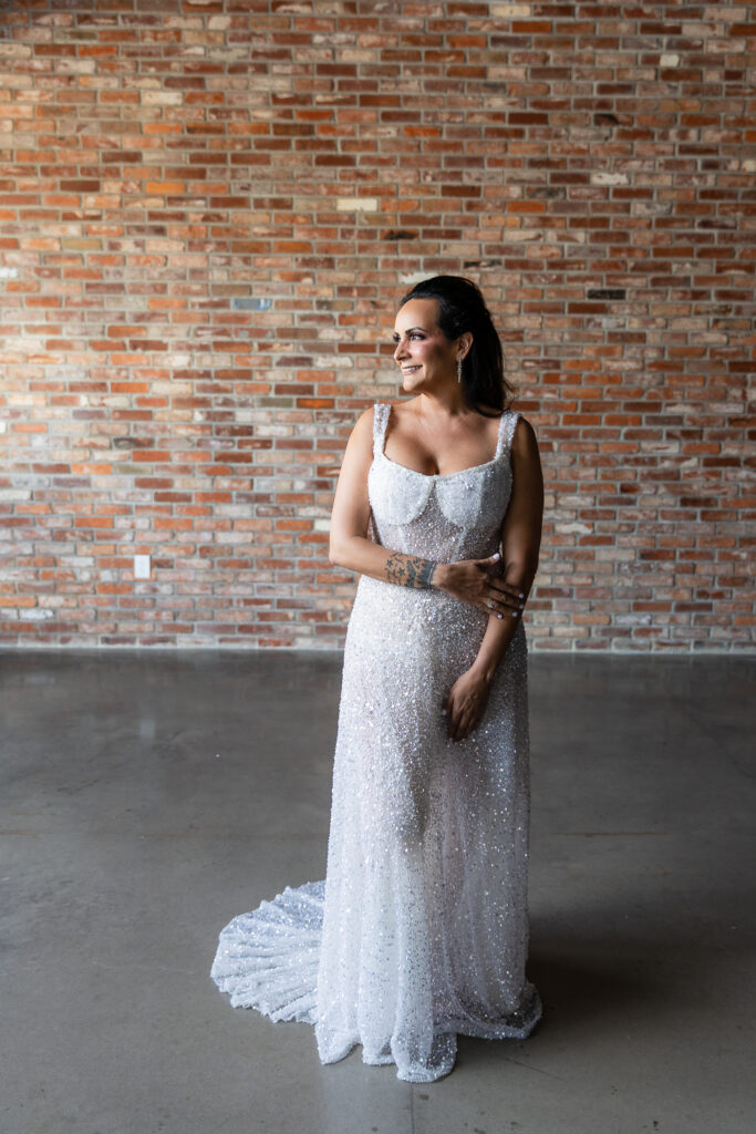 bride standing in front of brick wall in a Galia Lahav Oriana sparkling a-line wedding dress with a sweetheart neckline at Prosper Wine House in Prosper Texas