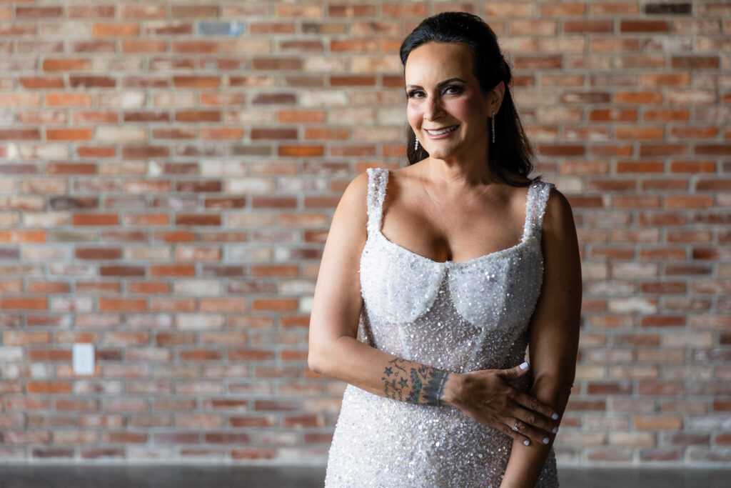 bride standing in front of brick wall smiling in a Galia Lahav Oriana sparkling a-line wedding dress with a sweetheart neckline at Prosper Wine House