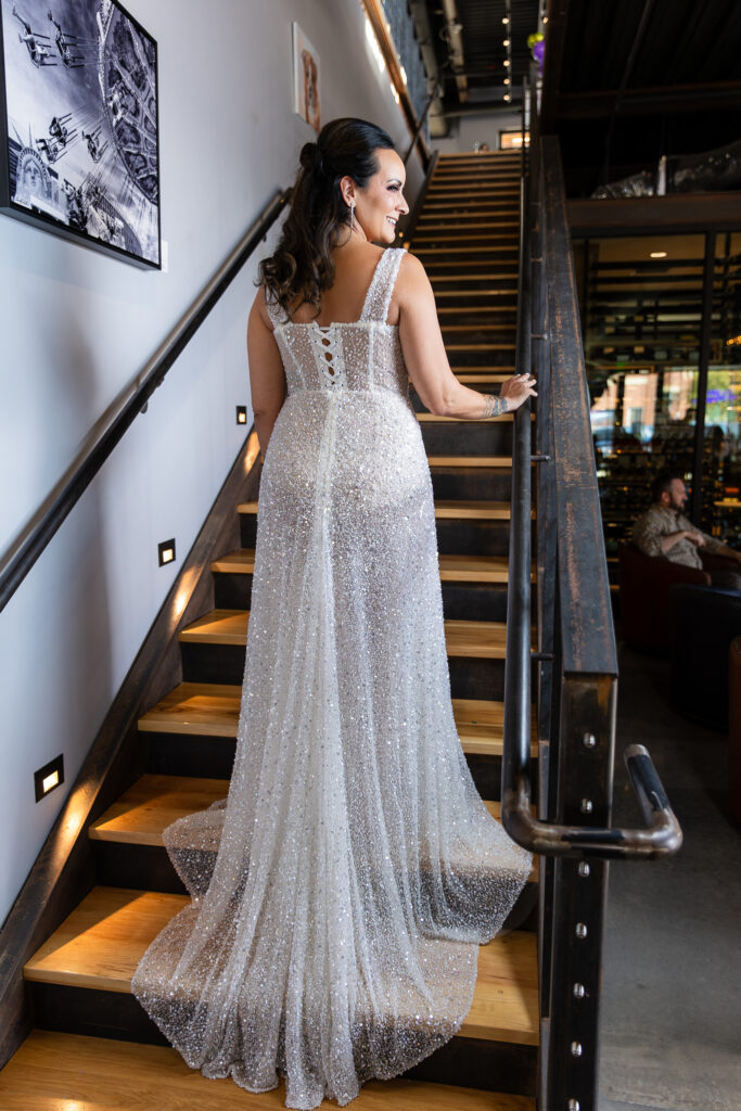 bride standing backwards on staircase smiling in a Galia Lahav Oriana sparkling a-line wedding dress with a sweetheart neckline at Prosper Wine House