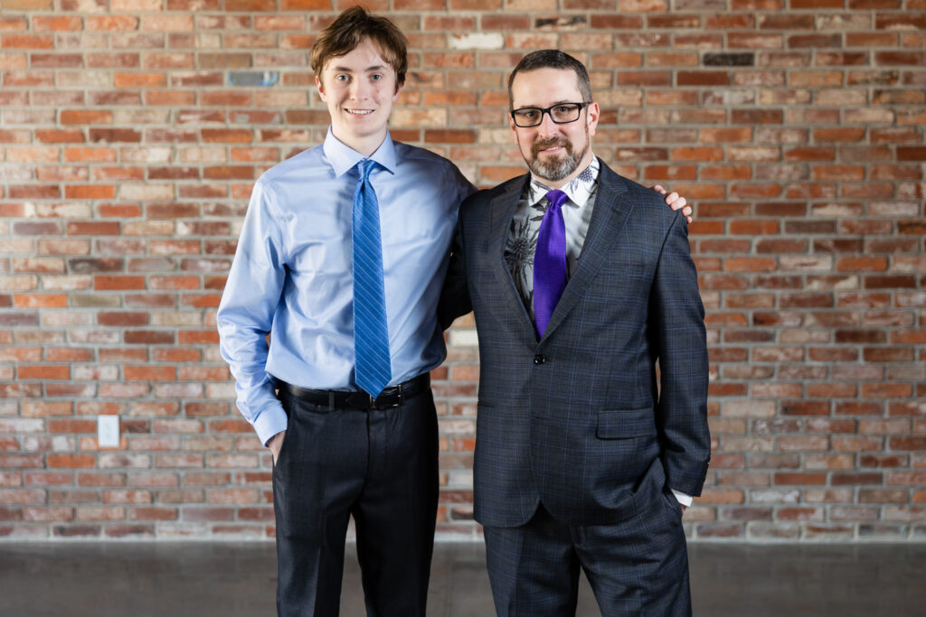 groom and son standing together in dark grey ted baker suits in front of brick wall