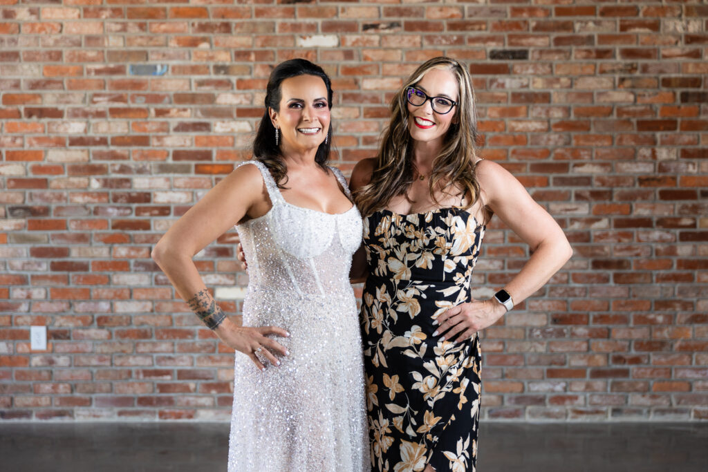 bride and friend smiling at camera in front of brick wall