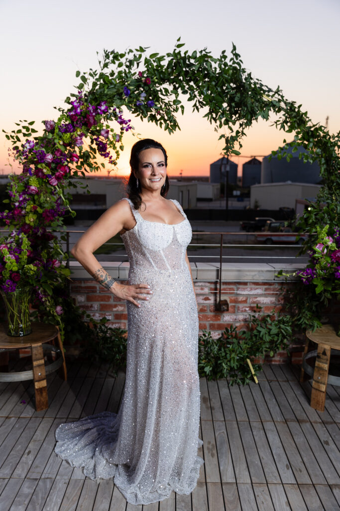 bride standing in front of floral arch on rooftop at sunset in a Galia Lahav Oriana sparkling a-line wedding dress with a sweetheart neckline at Prosper Wine House