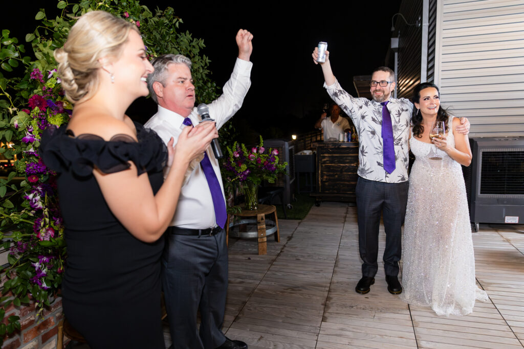 best man giving speech and toasting a laughing bride and groom during wedding reception on rooftop of Prosper Wine House