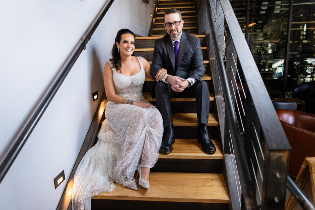 bride in a Galia Lahav Oriana sparkling a-line wedding dress sitting on staircase at Prosper Wine House with groom in dark grey ted baker suit smiling