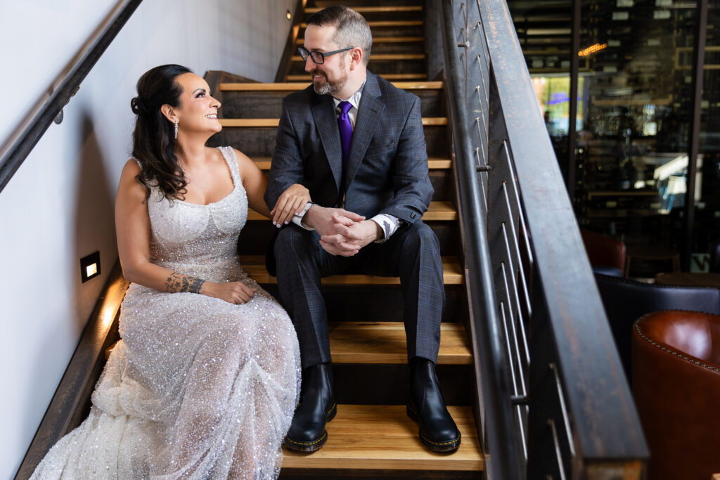 bride in a Galia Lahav Oriana sparkling a-line wedding dress sitting on staircase at Prosper Wine House with groom in dark grey ted baker suit smiling at each other