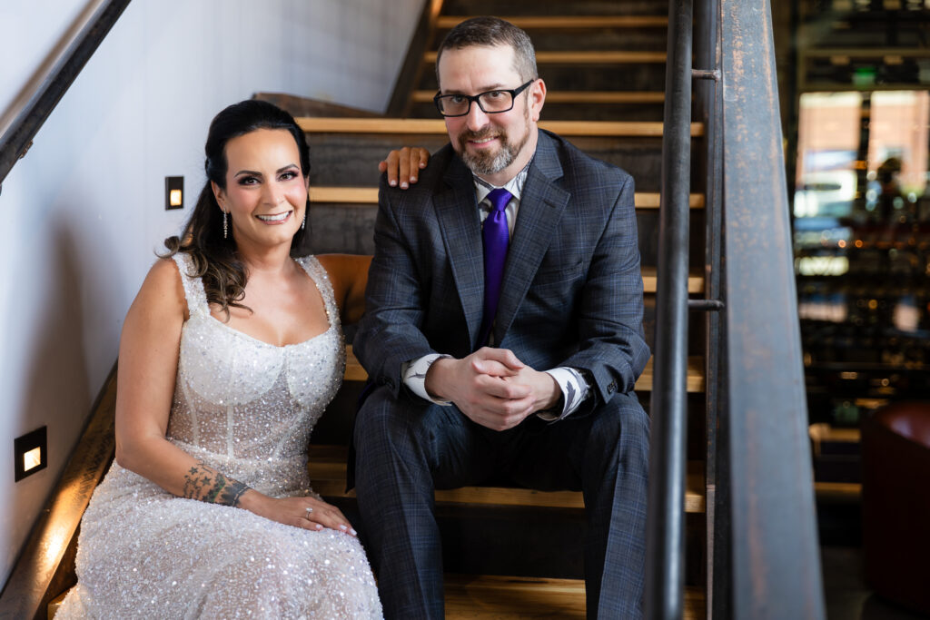 bride in a Galia Lahav Oriana sparkling a-line wedding dress sitting on staircase at Prosper Wine House with groom in dark grey ted baker suit smiling at camera