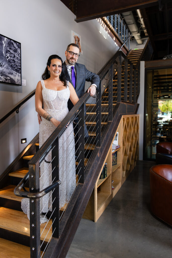 bride in a Galia Lahav Oriana sparkling a-line wedding dress standing on staircase at Prosper Wine House with groom in dark grey ted baker suit smiling at camera