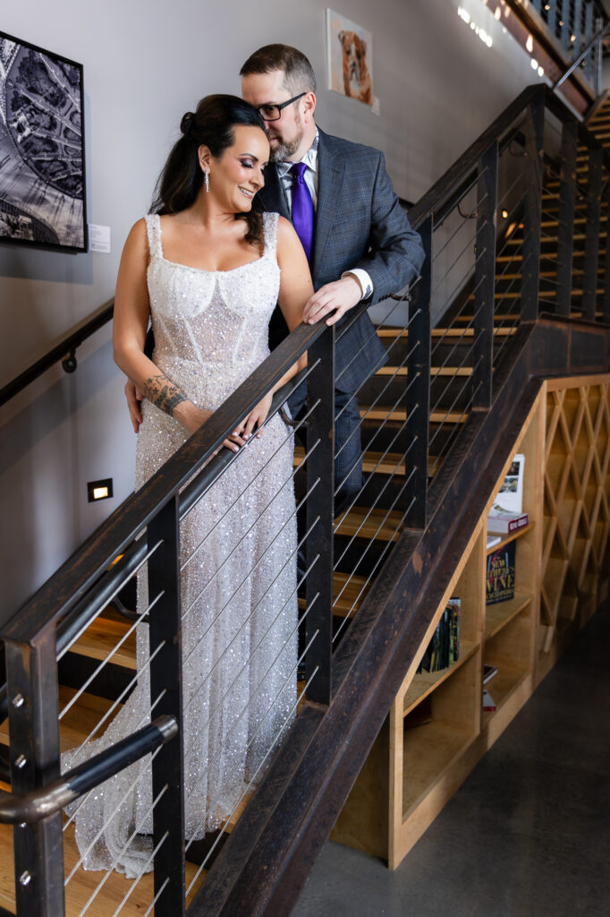 bride in a Galia Lahav Oriana sparkling a-line wedding dress standing on staircase at Prosper Wine House with groom in dark grey ted baker suit snuggling into each other