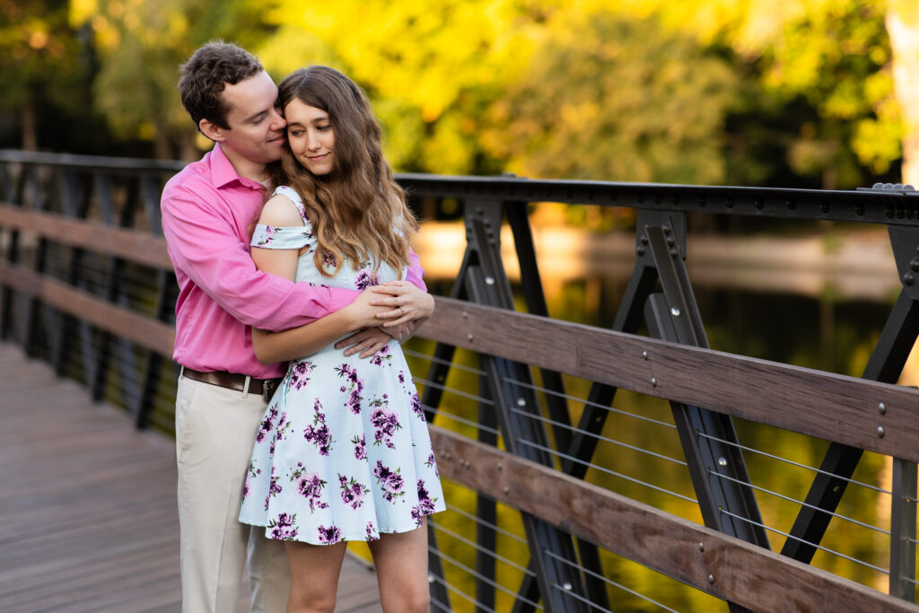 engaged couple snuggling and cuddling into each other on wood bridge during engagement session at lakeside park in Dallas