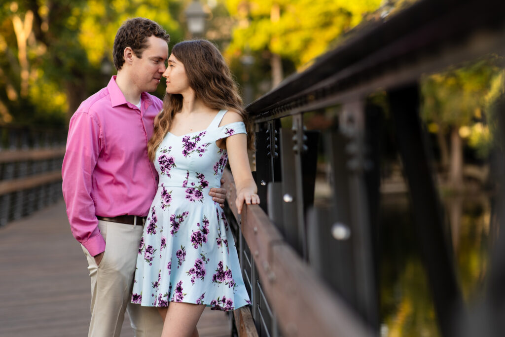 engaged couple forehead to forehead leaning against wooden bridge at lakeside park