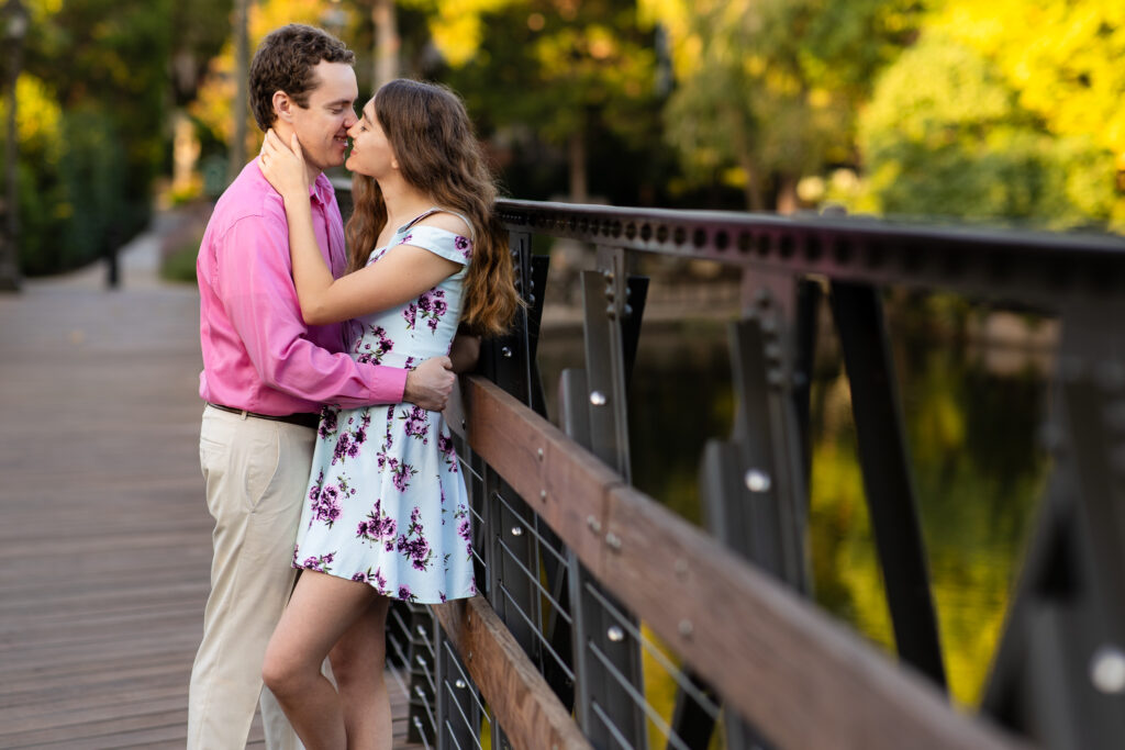 bride and groom smiling and going in for kiss on wood bridge at lakeside park during sunrise engagement session in dallas