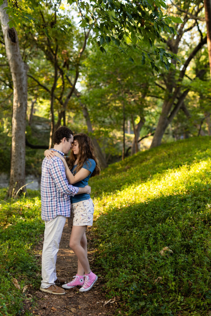 engaged couple standing forehead to forehead in the woods at Prather Park