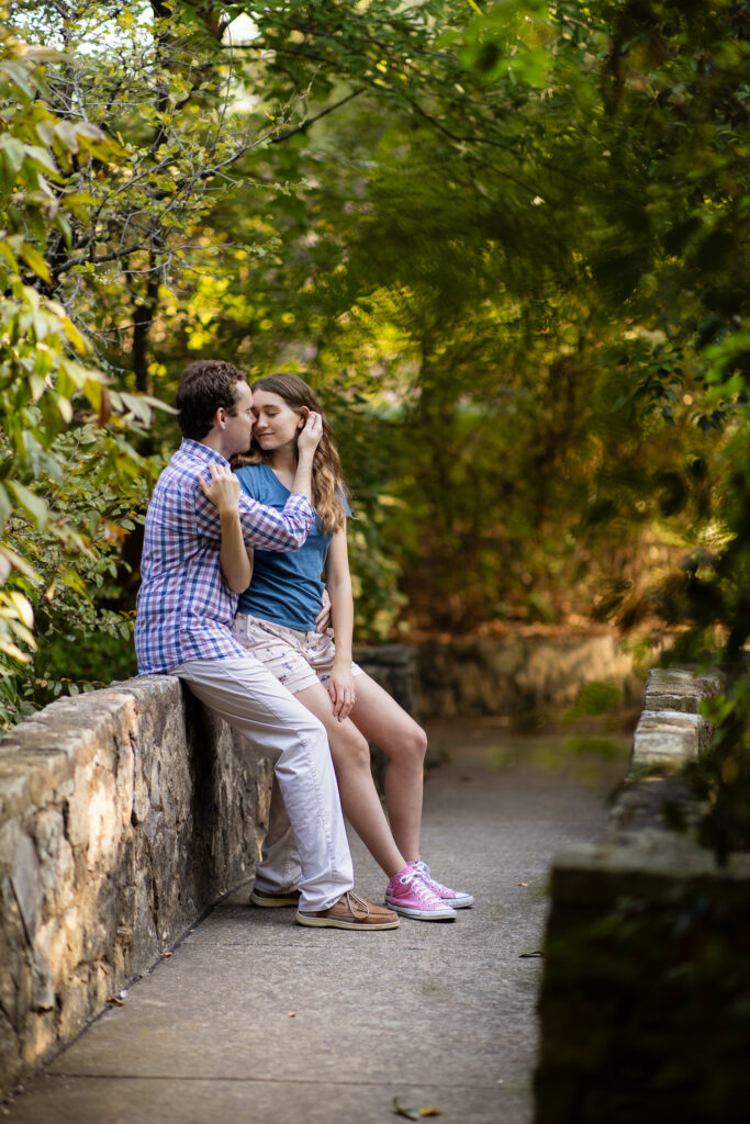 engaged couple intimately sitting on stone bridge wall at Prather Park