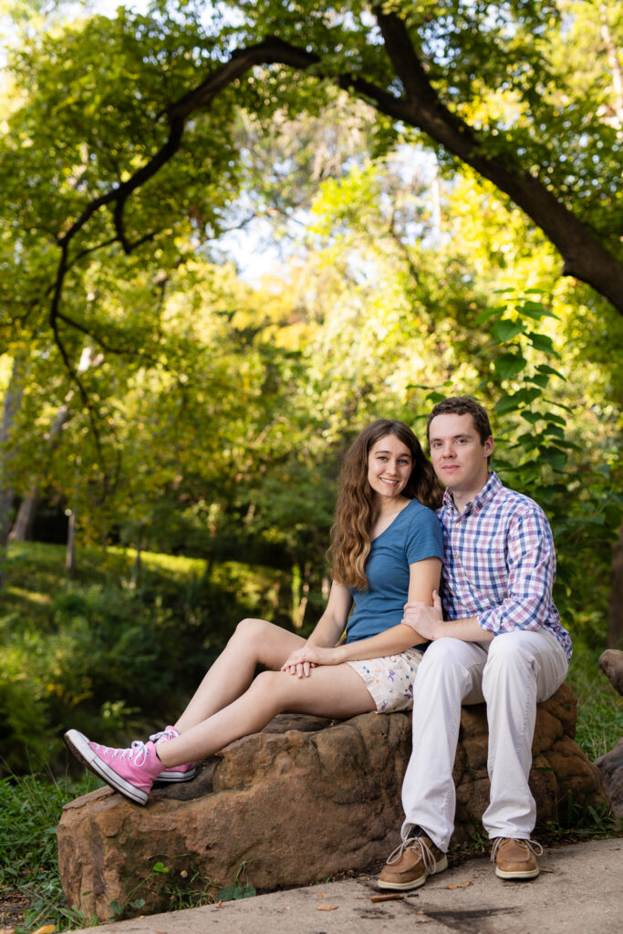 engaged man and woman sitting on rock with trees in the background at Prather Park during sunrise engagement session