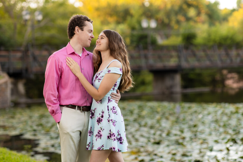 engaged couple smiling and embracing each other during sunrise lakeside park engagement session in Dallas TX